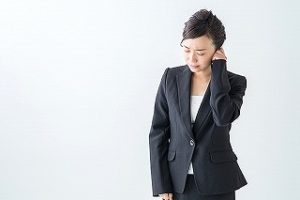 寝違えで通勤中に首を押さえるスーツ姿の女性